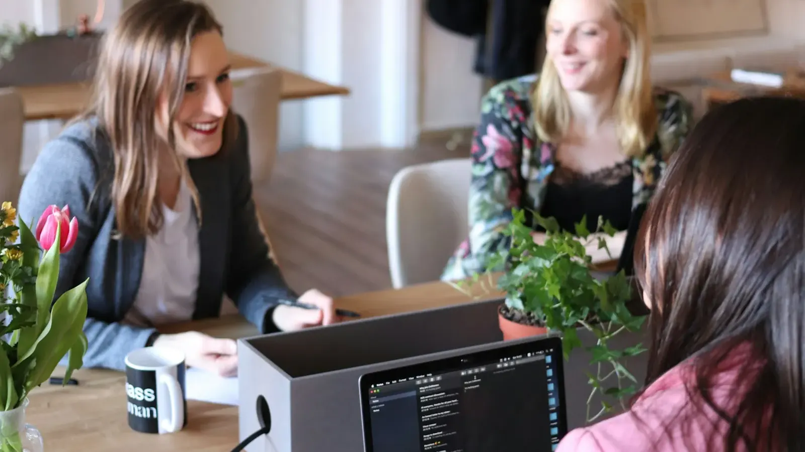 Drei Kollegen lachen und besprechen am Tisch Daten auf einem Laptop.