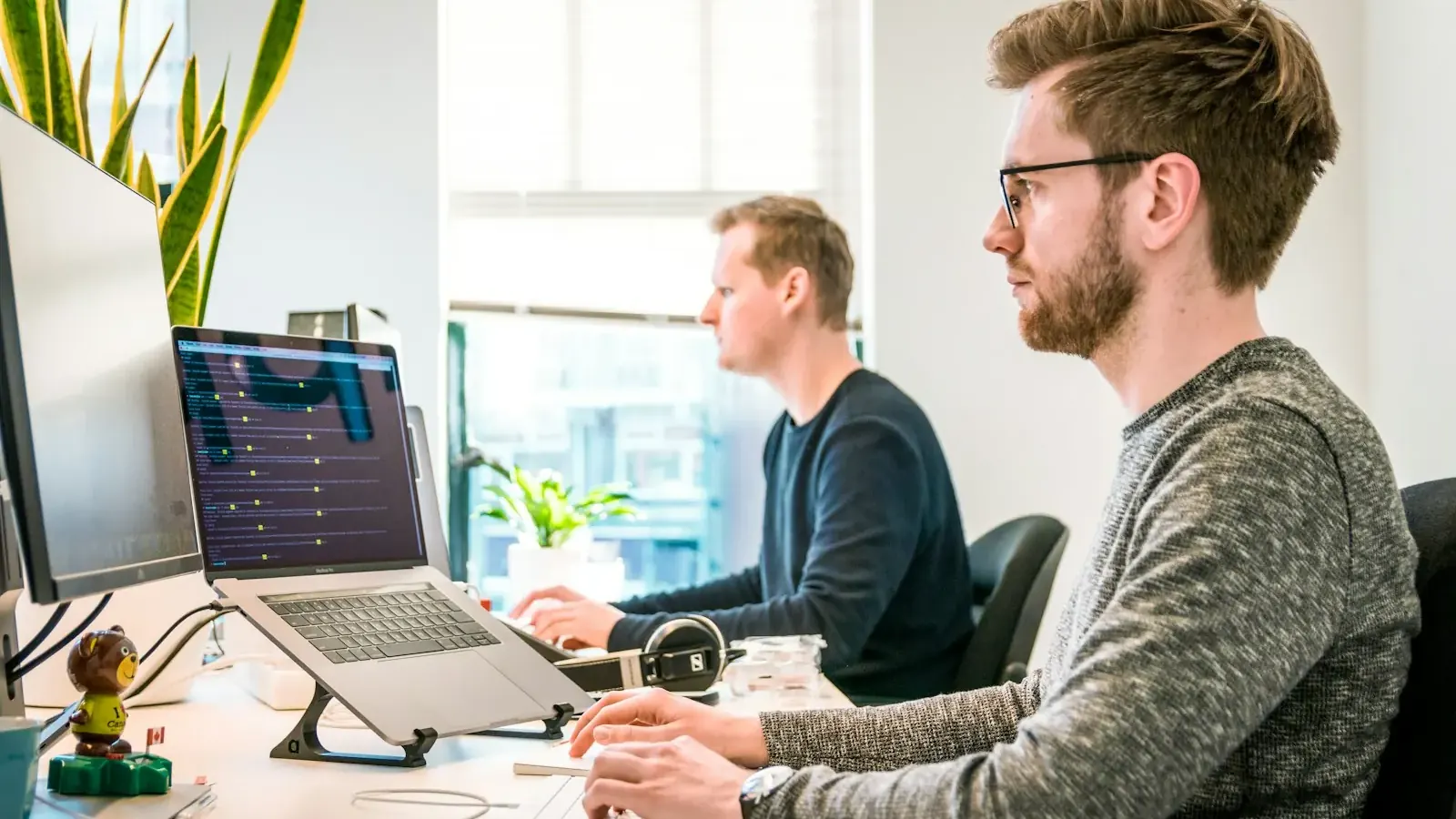 Zwei Entwickler arbeiten nebeneinander an ihren Laptops in einem hellen Büro.