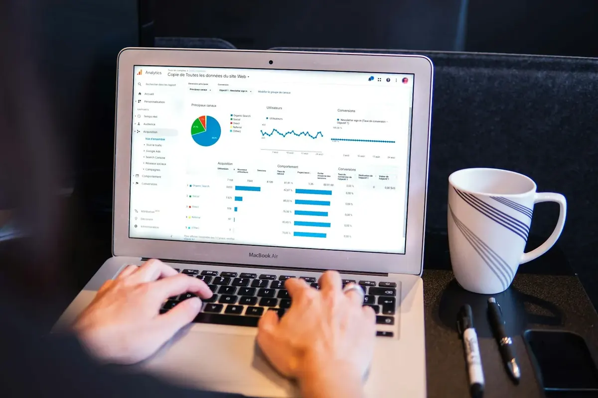 Hände tippen an einem Laptop mit Analytics-Diagrammen, daneben steht eine Tasse.