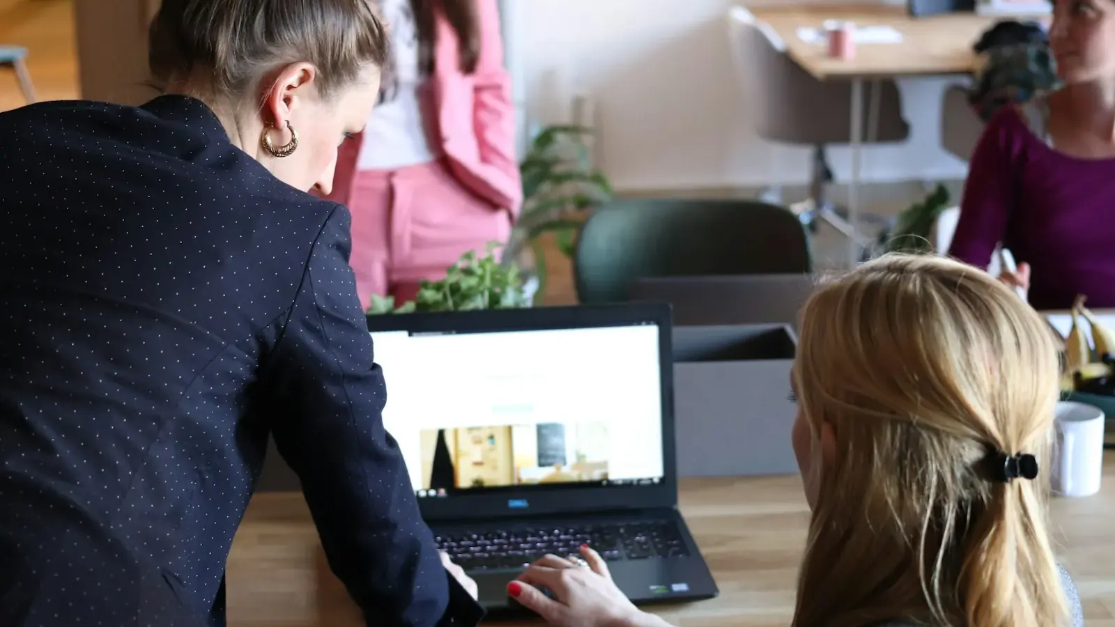 Zwei junge Frauen betrachten über die Schulter hinweg eine Webseite auf dem Laptop.