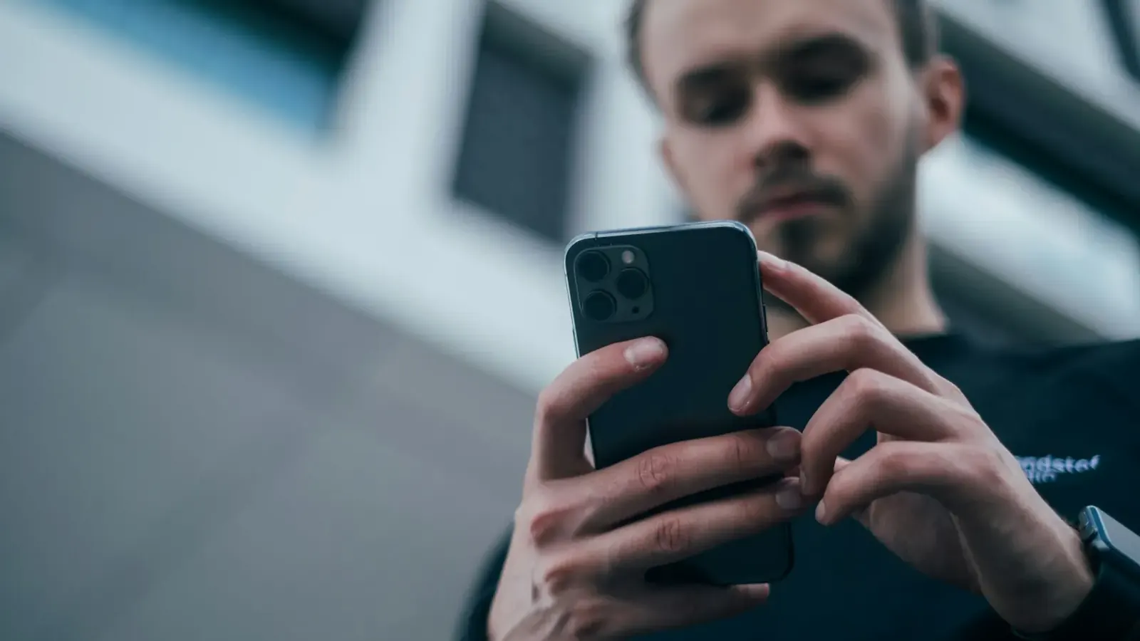 Ein junger Mann schaut aus dynamischer Froschperspektive auf sein Smartphone.