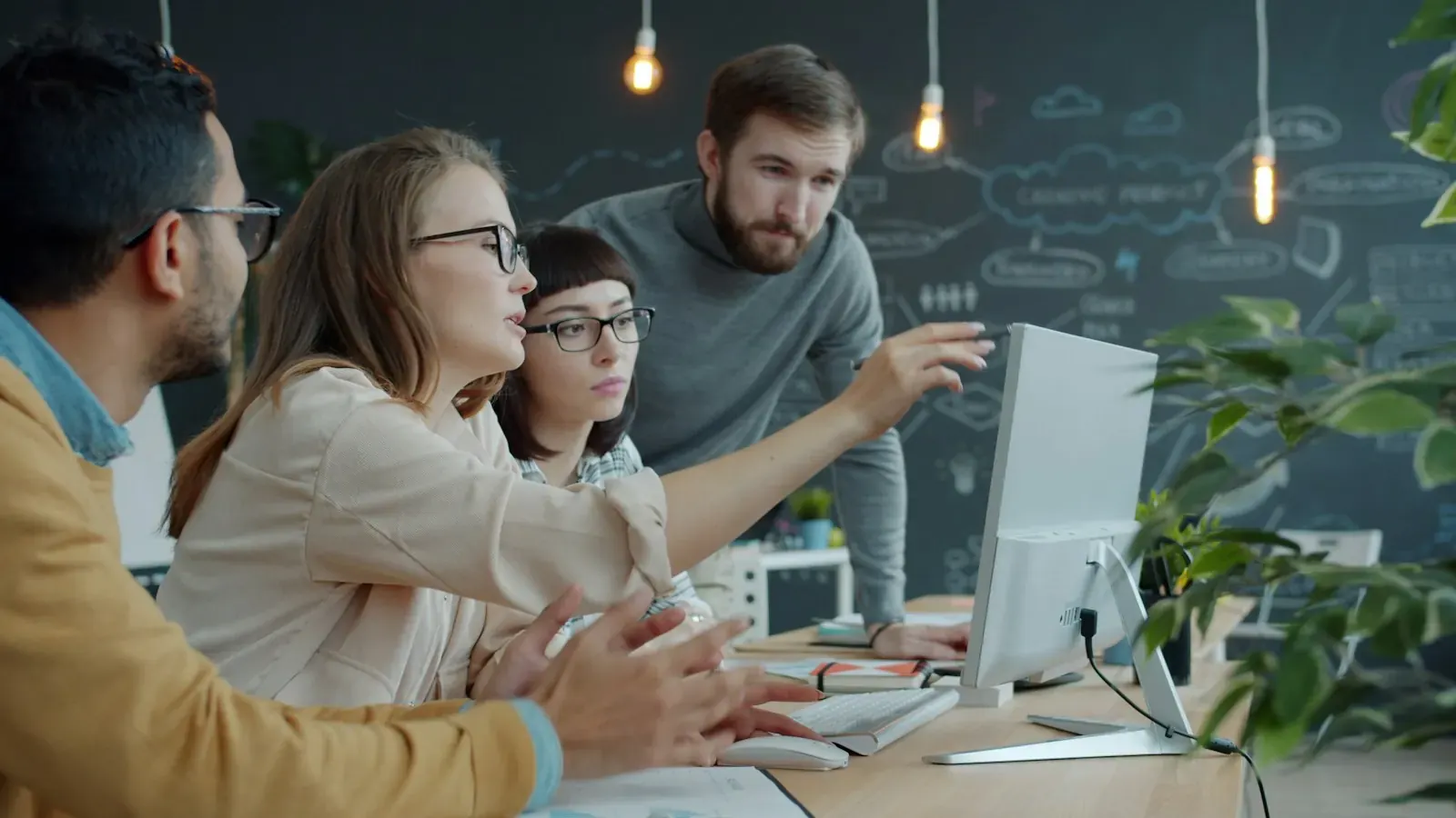 Ein Team bespricht Ergebnisse auf einem Monitor vor einer Kreidewand.