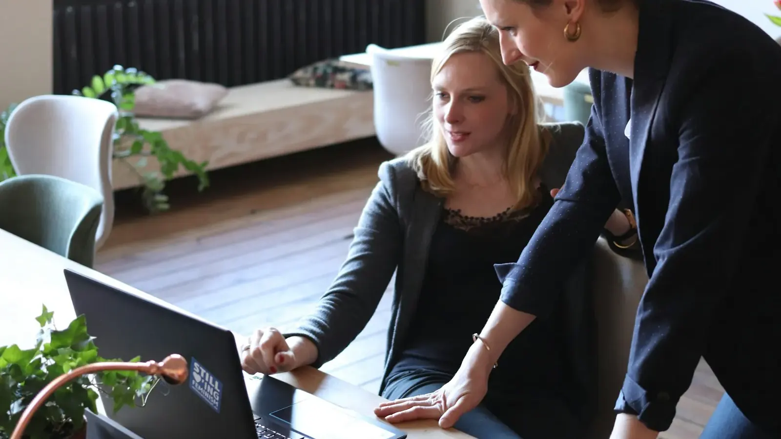Eine Frau zeigt ihrer Kollegin eine Arbeit am Laptop in einem hellen Coworking-Space.
