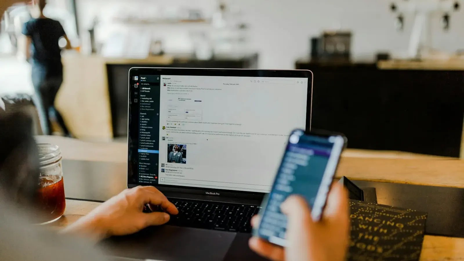 Hands hold a smartphone and a laptop at once, showing a feed and a website.