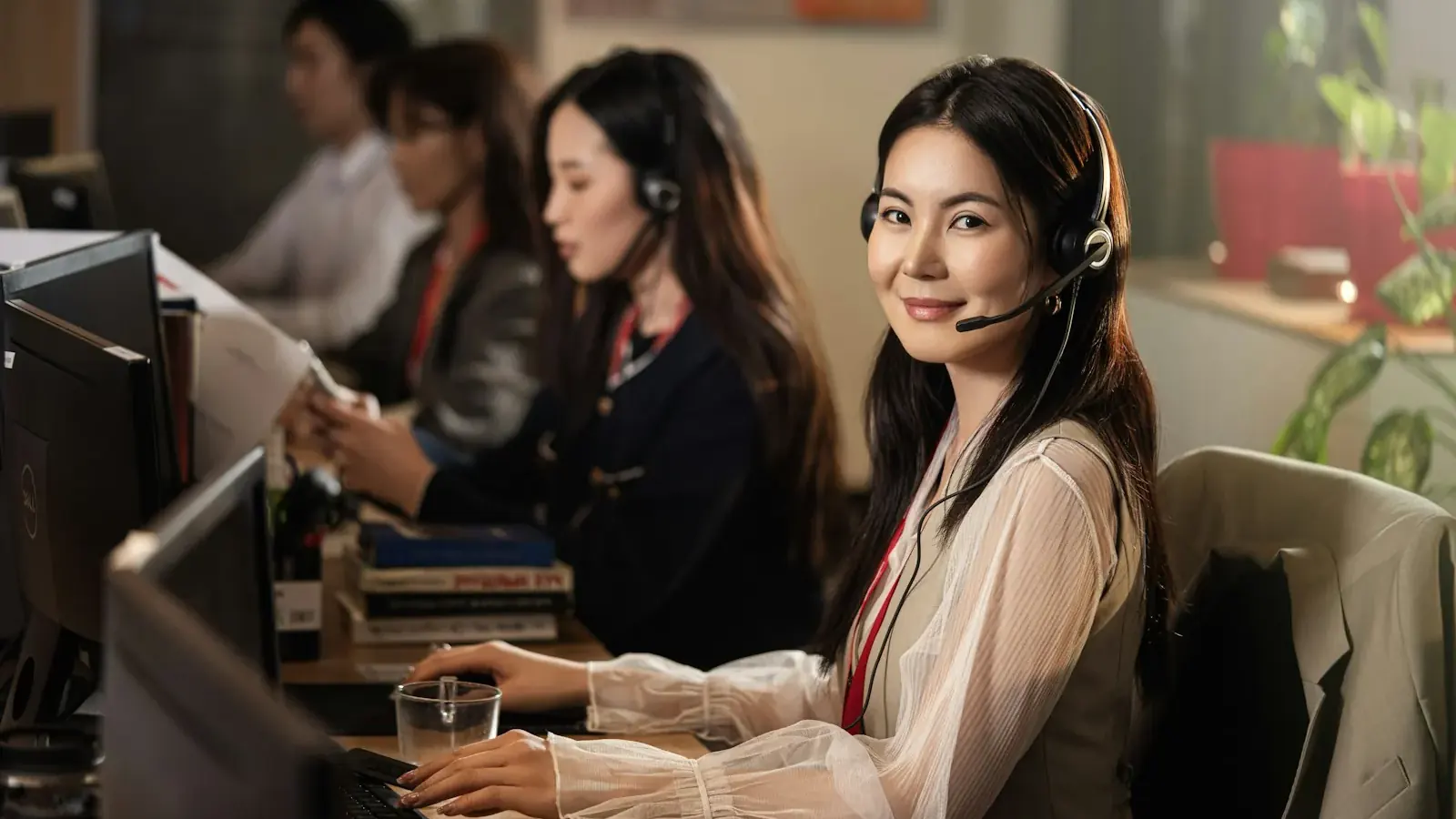 A smiling support operator in a headset sits among colleagues at their computers.
