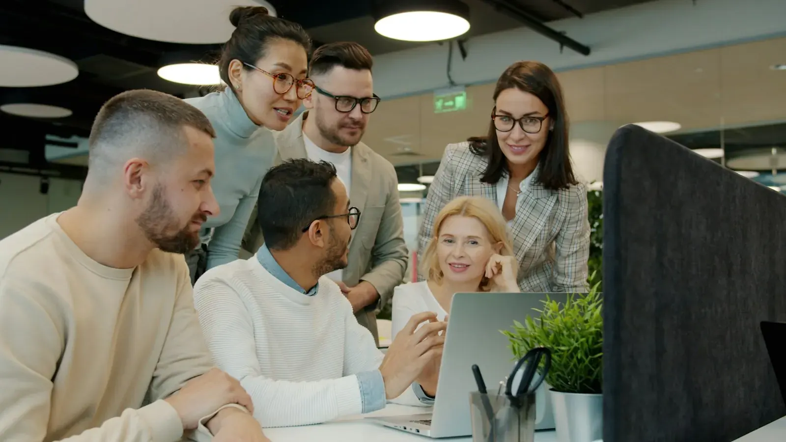 A diverse team leans over a laptop and discusses a workflow.