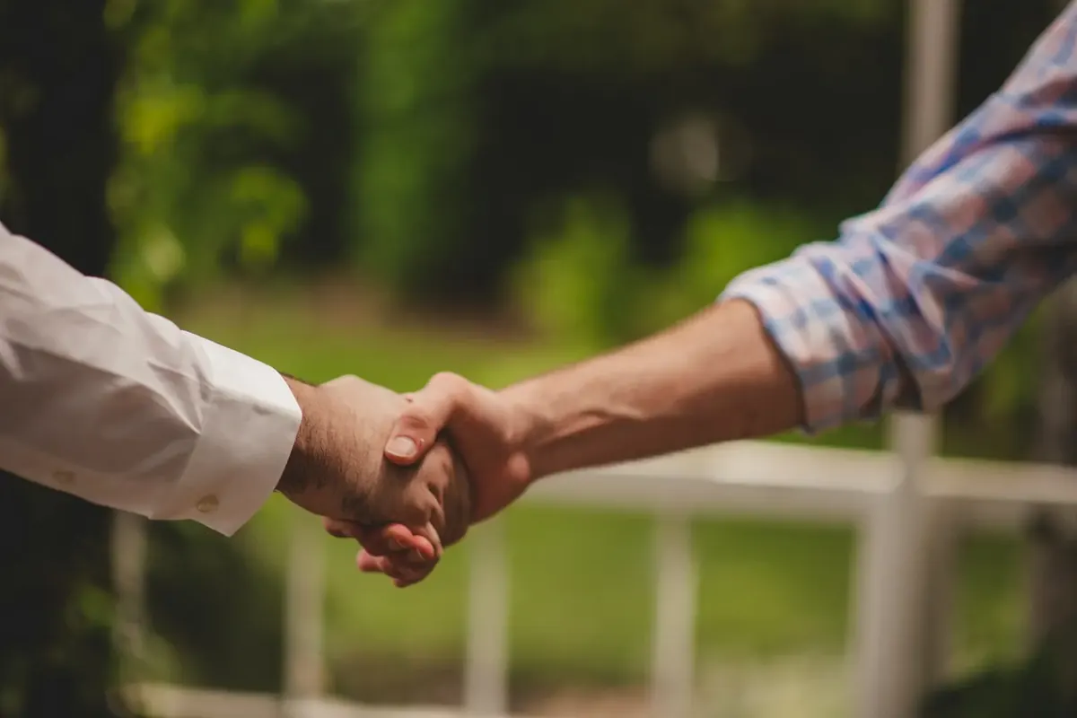 A close-up handshake between two people against lush greenery seals an agreement.