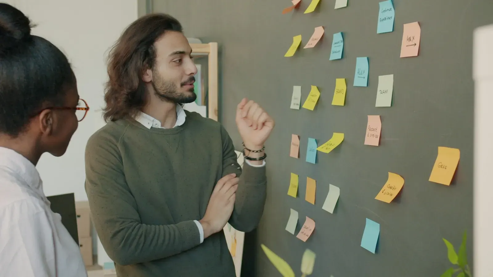 A woman and a man discuss a project plan at a wall covered with sticky notes.