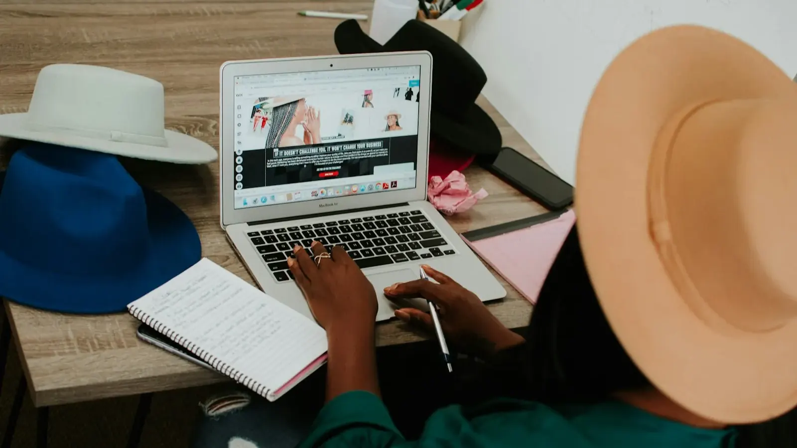 A hat workshop owner works on a laptop, building a website for her small business.