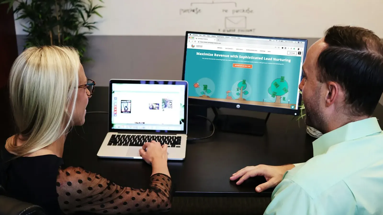 A woman and a man review a landing page on a large monitor and a laptop.