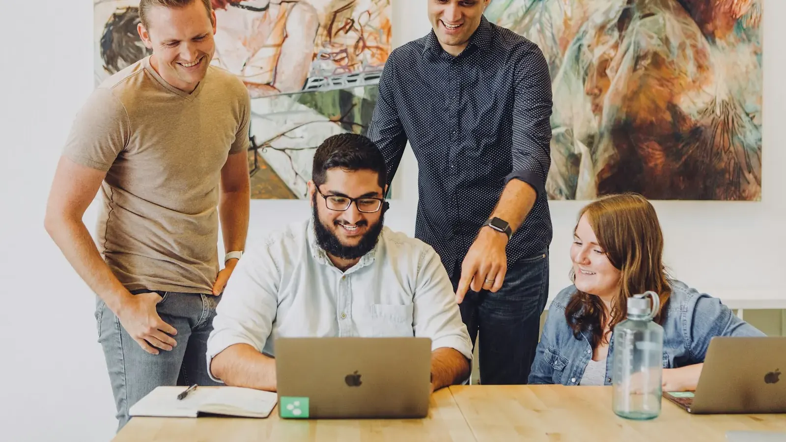 A startup team celebrates a result around a laptop in an office.
