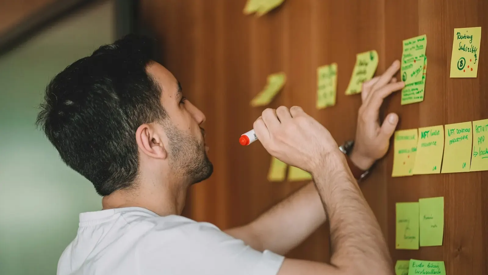 Un hombre con un rotulador coloca notas adhesivas con el plan del proyecto en una pared.