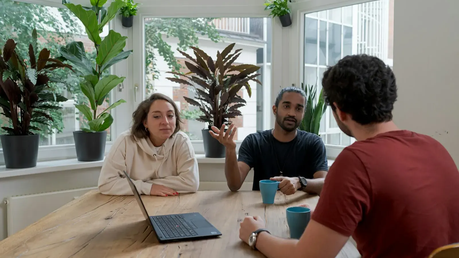 Tres compañeros comentan con entusiasmo un producto en una mesa de una oficina luminosa.