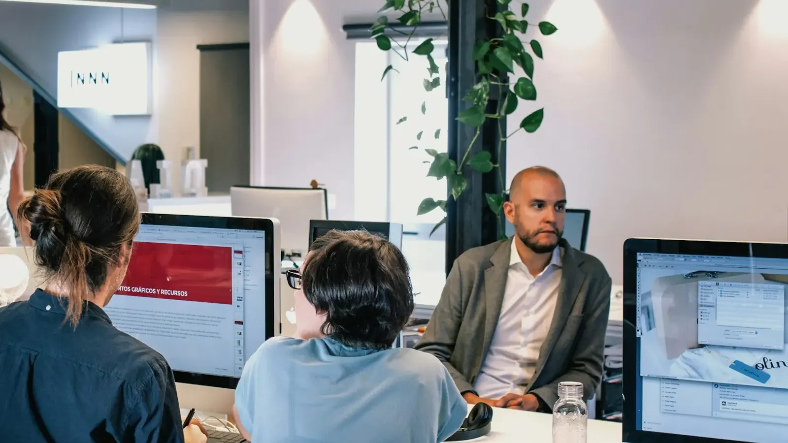 Un equipo de una agencia ante varios monitores: la responsable explica el proyecto a unos clientes.
