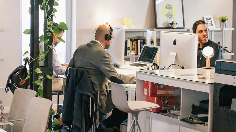 Um programador de auscultadores trabalha num computador, com um colega ao lado.