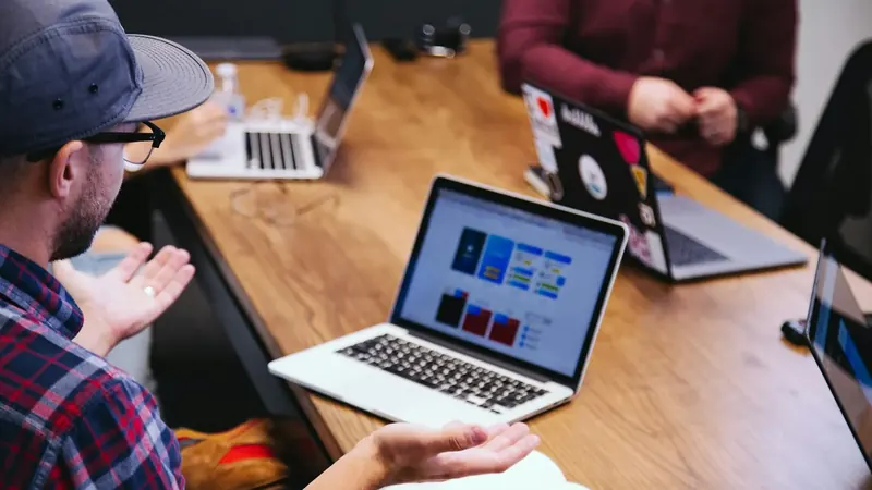 Um designer de boné explica a maquete num portátil à equipa à mesa.
