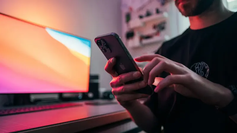 Um homem desliza o ecrã do telemóvel diante de um monitor rosa e laranja muito vivo.