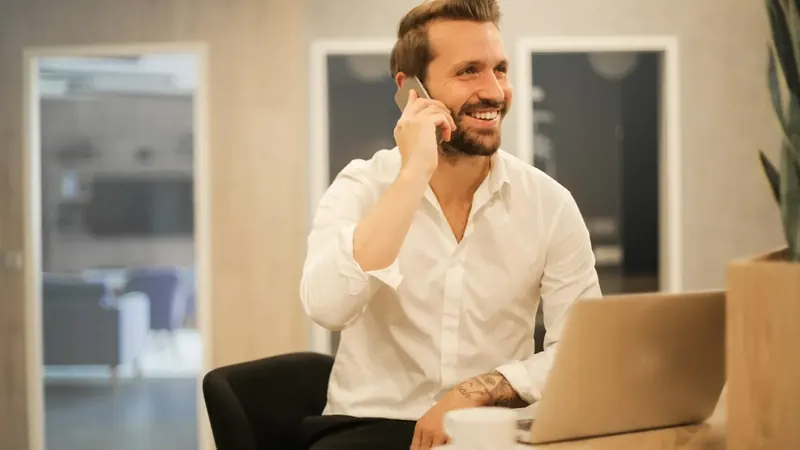 Um homem sorridente atende o telefonema de um cliente ao portátil, num escritório.