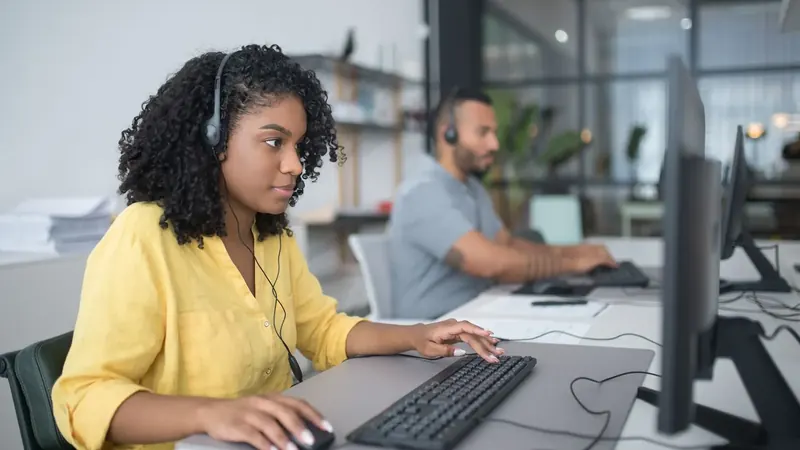 Um operador de apoio com auricular responde a clientes ao computador.