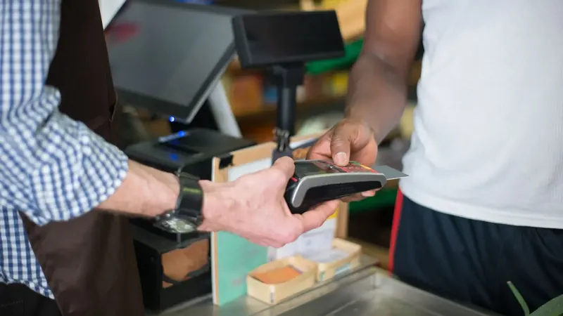 Um cliente paga com cartão no terminal da caixa de uma loja.